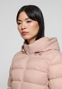 Jasnoróżowa kurtka ocieplana z zamkiem z przodu, regulowanym kapturem i przeszytymi panelami. Gładka tekstura z minimalnymi akcentami sprzętowymi.