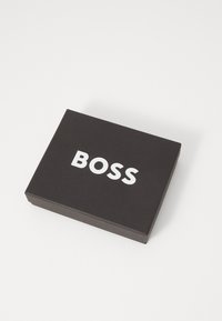 Boîte rectangulaire noire avec une texture lisse, portant le mot "BOSS" en lettres blanches en gras sur la surface supérieure.