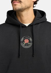 Black hoodie featuring a drawstring hood and a central graphic patch with a rose design in red and green, set against a circular background.