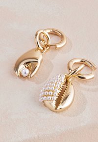 Örhängen i guldfärg med snäckskaldesign. Den ena pryds av en pärla inuti, och den andra är dekorerad med små vita pärlor.