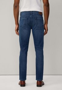 Dunkelblaue Denim-Jeans im Slim-Fit-Design, mit fünf Taschen und einem Leder-Label auf dem Taillenbund, von hinten betrachtet.