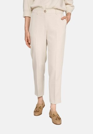 Pantalon beige ajusté avec une coupe droite, doté d'une fermeture à bouton, de poches latérales et de plis à l'avant. Une paire de mocassins marron est présentée.