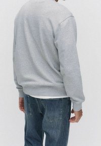 Sweat-shirt gris en mélange de coton, avec manches longues, col rond et coupe décontractée. Associé à un jean en denim bleu.