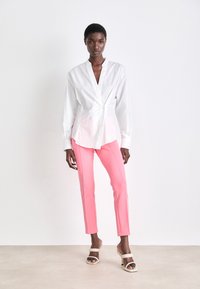 White button-up shirt with a deep V-neck, paired with pink slim-fit pants and beige high-heeled sandals. Smooth textures and crisp lines.