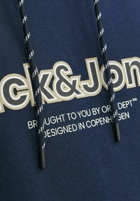 Sudadera azul marino con un gran logotipo en crema y negro, con un cordón que tiene un patrón de rayas en blanco y negro y extremos de plástico.