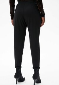 Zwarte op maat gemaakte broek met een slim fit, met een gladde textuur en opgerolde zomen, gecombineerd met zwarte stiletto laarzen voor een elegante uitstraling.