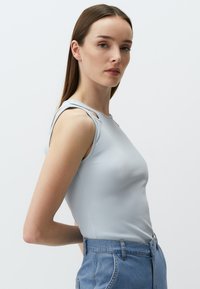 Top in cotone azzurro chiaro a coste con dettagli scollati sulle spalle, abbinato a jeans in denim a vita alta, che mettono in evidenza un design aderente.