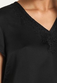 Blusa nera con scollatura a V. Presenta dettagli in pizzo testurizzato attorno al collo. Tessuto morbido con una finitura liscia. Maniche corte.