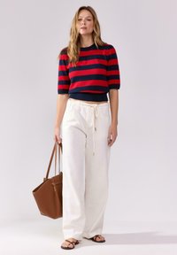 Červený a námořnický pruhovaný zkrácený svetr, bílé kalhoty s širokými nohavicemi a šňůrkou, hnědá kabelka a černé žabky. Hladké textury, ležérní design.