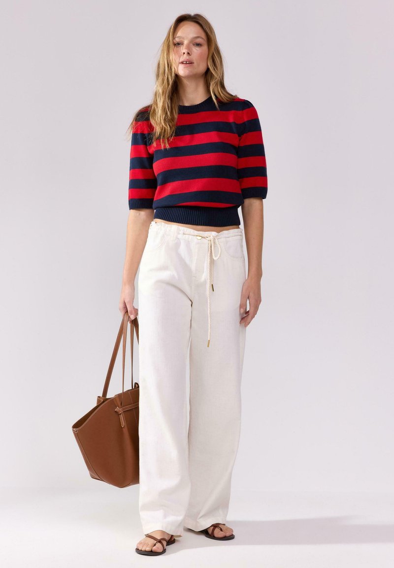 Červený a námořnický pruhovaný zkrácený svetr, bílé kalhoty s širokými nohavicemi a šňůrkou, hnědá kabelka a černé žabky. Hladké textury, ležérní design.