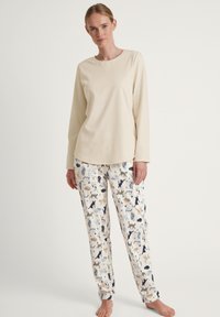 Maglietta da pigiama a maniche lunghe color crema abbinata a pantaloni leggeri e fantasia con illustrazioni di vari animali in tonalità blu e beige.