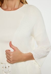 Cardigan bianco realizzato in un leggero tessuto a maglia, caratterizzato da un ampio davanti aperto e maniche a ¾ con una finitura testurizzata.
