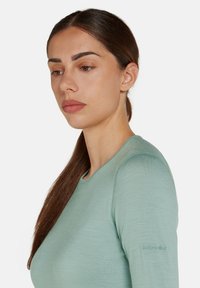 Camicia a maniche lunghe verde chiaro realizzata in materiale morbido; presenta un colletto rotondo e un logo ricamato sulla manica sinistra.