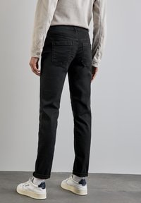 Svarta denimjeans med rak passform, synliga fickor och lätt blekning. Matchas med vita sneakers som har en mörkblå accent.