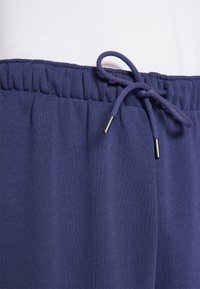Navy blue sweatpants with elastic waistband and drawstring, featuring a smooth texture and metallic aglets on the drawstring ends.