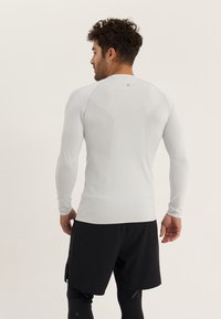 Langärmliges Sportoberteil in Hellgrau mit perforierter Textur auf dem Rücken, kombiniert mit schwarzen Shorts, die ein figurnahes Design zeigen.