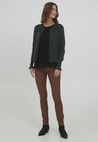 Tamnozelena kardigan s teksturiranim okovratnikom, crni plisirani top ispod, smešaste uske hlače i crne gležnjače. Jednostavan i elegantan dizajn.