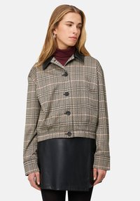 Blousejack met een geruit patroon in beige en zwarte tinten, een zwarte leren kraag en een cropped design over een zwarte leren rok.