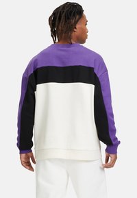 Felpa color block in viola, nero e bianco. Presenta una vestibilità rilassata, polsini a coste e un morbido tessuto misto cotone.