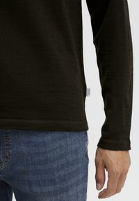 Tumedatest rohelisest pikast varrukast särgist, mis on valmistatud tekstuuriga kangast, otse allääre ja väikese kaubamärgi sildiga küljel, koos siniste teksadega.