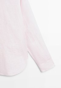 Polsino e orlo di camicia a manica lunga a righe verticali rosa chiaro e bianco su sfondo bianco.