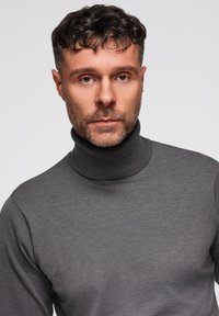 Maglione grigio a collo alto in tessuto a maglia, caratterizzato da un collo alto e una vestibilità aderente, indossato da un modello su uno sfondo neutro.