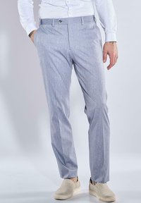 Hellgraue, maßgeschneiderte Hose mit dezentem Muster, seitlichen Taschen und flacher Vorderseite. Kombiniert mit cremefarbenen Slippern.