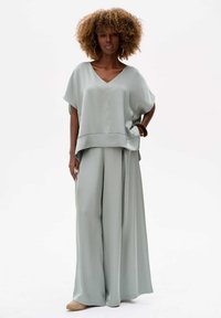 Lichtgroene satijnen twee-delige outfit met een ontspannen V-hals top en brede broek, met een gladde textuur en vloeiende drape.