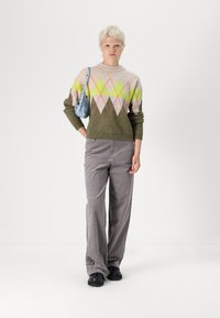 Knit sweater with a geometric pattern in pink, green, and beige; olive green body. Gray wide-leg pants, black shoes, and a small blue handbag.