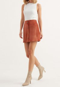 Ribbad vit linne med en mini kjol i rustfärgad kordflossa som har sju knappar fram. Modellen bär beiga klackade ankelskor.