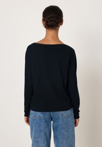 Svart långärmad topp med bred halsringning, med en avslappnad passform. Kombinerad med ljusblå högmidjade jeans med synliga bakfickor.