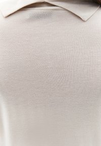 Lichtbeige polo shirt met een zachte textuur, voorzien van een klassieke kraag en een glad, gelijkmatig oppervlak zonder patronen of versieringen.