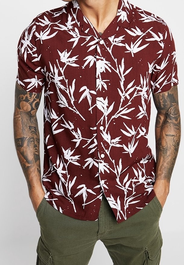 Camicia corta a maniche corte di color bordeaux con motivo di foglie di bambù bianche, design con bottoni e tessuto leggero. Abbinata a pantaloni cargo verdi.
