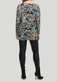 Haut à manches longues avec un motif abstrait multicolore en nuances de bleu, beige et noir, associé à un legging en cuir noir ajusté.