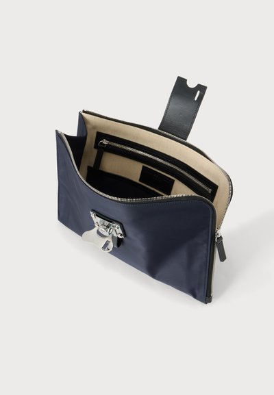 Pochette rectangulaire bleu marine ouverte, dévoilant l'intérieur en tissu beige avec une poche zippée noire et une fermeture métallique argentée à l'avant.