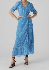 Ljusblå klänning i genomskinligt tyg med vita prickar, volangkant vid halsen, pufferade ärmar och en flerlagers fåll. Bärs med bruna klacksandaler.