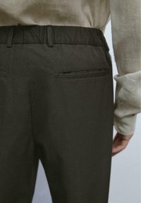 Donkere stoffen broek met een geplooide tailleband, zijzakken en een gladde textuur, gecombineerd met een licht, gestructureerd shirt.