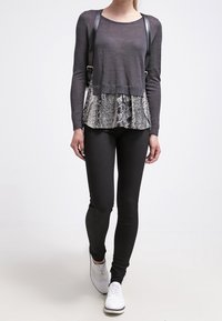 Gray long-sleeve top with snake print peplum, paired with black leggings and white sneakers. Features shoulder straps and a relaxed fit.