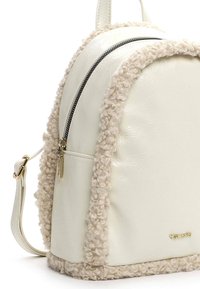 Sac à dos en simili cuir blanc avec des bordures en fausse fourrure beige texturée, doté d'une fermeture à double zip et d'un accent de marque en ton doré.