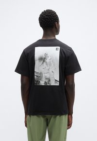 Μαύρο βαμβακερό t-shirt με μεγάλο μονόχρωμο γραφικό τύπωμα στην πλάτη, με μικρό λογότυπο στην πάνω γωνία.