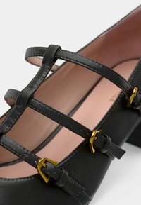 Black leather shoe with buckle-accented straps, featuring a low heel and a smooth, textured surface with a soft pink interior.