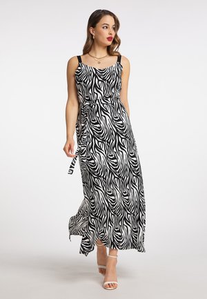 Vrouw die loopt, gekleed in een zwart-witte zebra print mouwloze maxi jurk met dunne bandjes en witte hoge hakken.