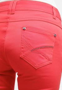 Jeans de denim rosa con un bolsillo trasero decorado con costuras y strass, textura suave y un diseño ajustado.