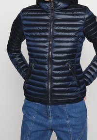 Giubbotto puffer blu navy con motivo a righe orizzontali, chiusura con zip e tasche laterali. Presenta un colletto alto e un tessuto liscio e lucido.
