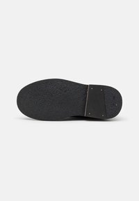 Semelle de chaussure en caoutchouc noir avec une surface texturée. Le talon présente une section rectangulaire noire avec quatre clous dorés pour le renforcement.