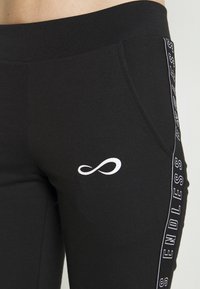 Svart sweatpants med en slät textur, med en vit oändlighetssymbol och texten "ENDLESS" längs sidan. Inkluderar sidofickor.