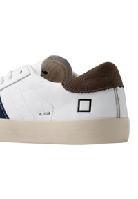 Sneaker bianca bassa con tallone in pelle marrone, striscia blu navy, suola crema e piccolo testo "HL/CLF" vicino alla cucitura laterale.