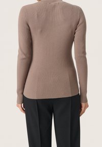 Top a maniche lunghe a coste di colore marrone chiaro, caratterizzato da un design aderente con collo alto e orlo leggermente curvo, abbinato a pantaloni neri.