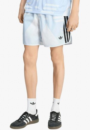 Persona che indossa pantaloncini Adidas azzurri con strisce nere, calzini bianchi Adidas e sneaker Adidas nere.