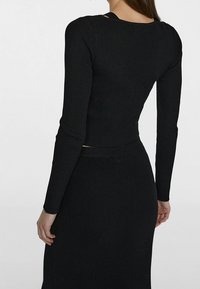 Haut noir à manches longues côtelé avec une coupe ajustée et un large décolleté orné d'une découpe dans le dos.